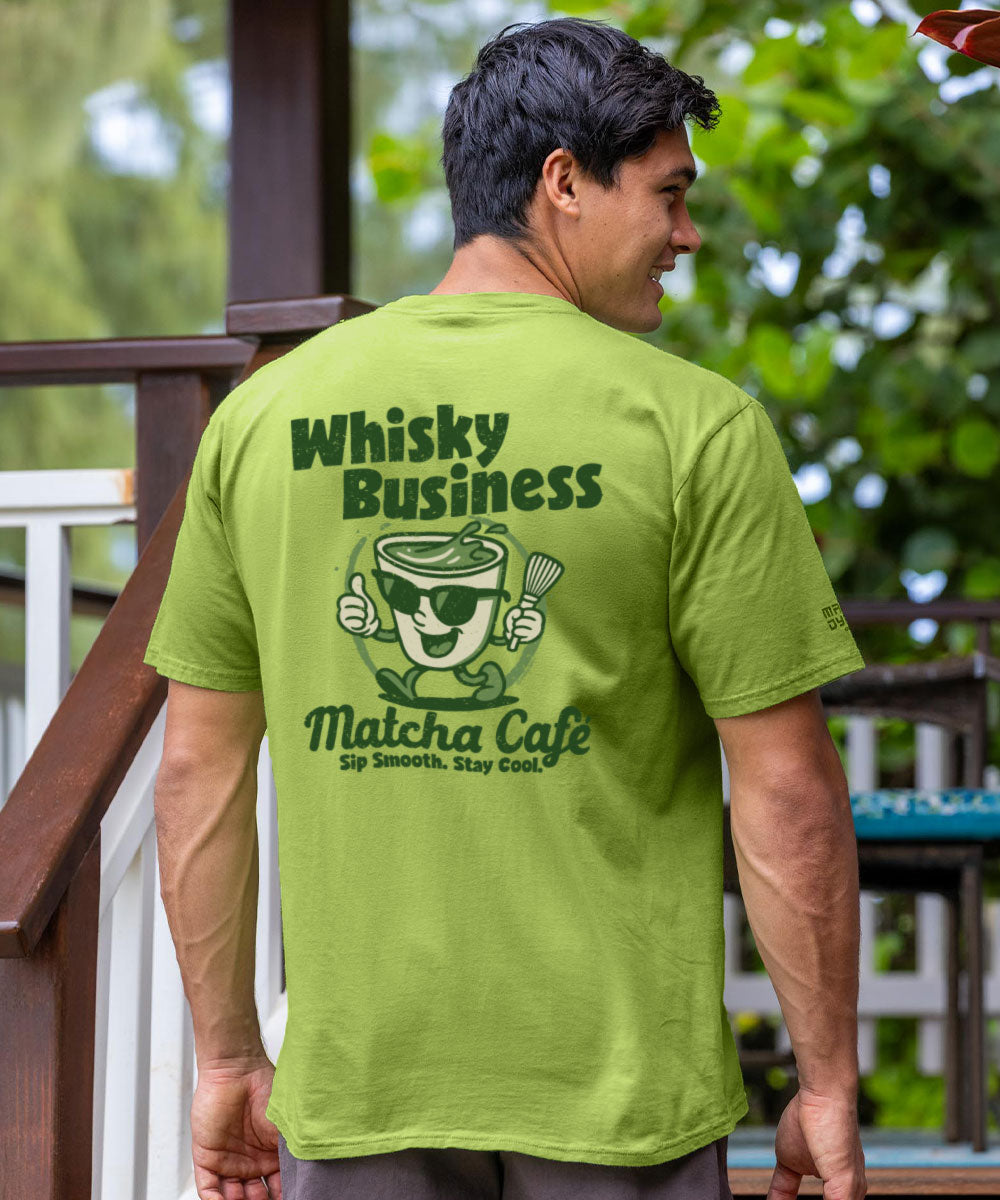 Person wearing a green t-shirt with 'Whisky Business Matcha Cafe' design outdoors. View 2