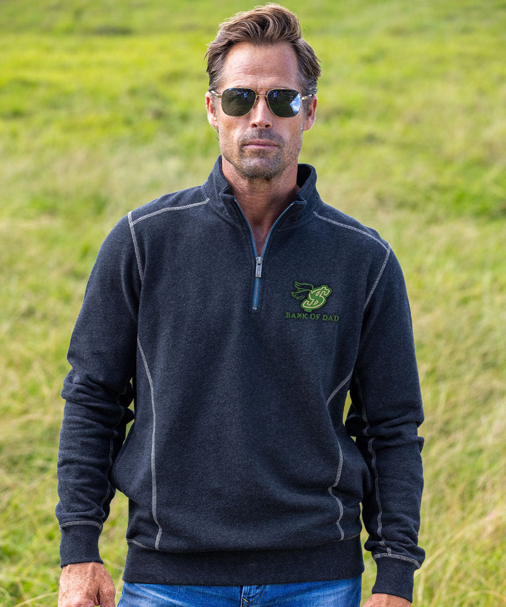 A man wearing a dark charcoal gray quarter-zip fleece pullover with a green and white 'Bark of the Dog' logo on the left chest, standing in a grassy field. View 2