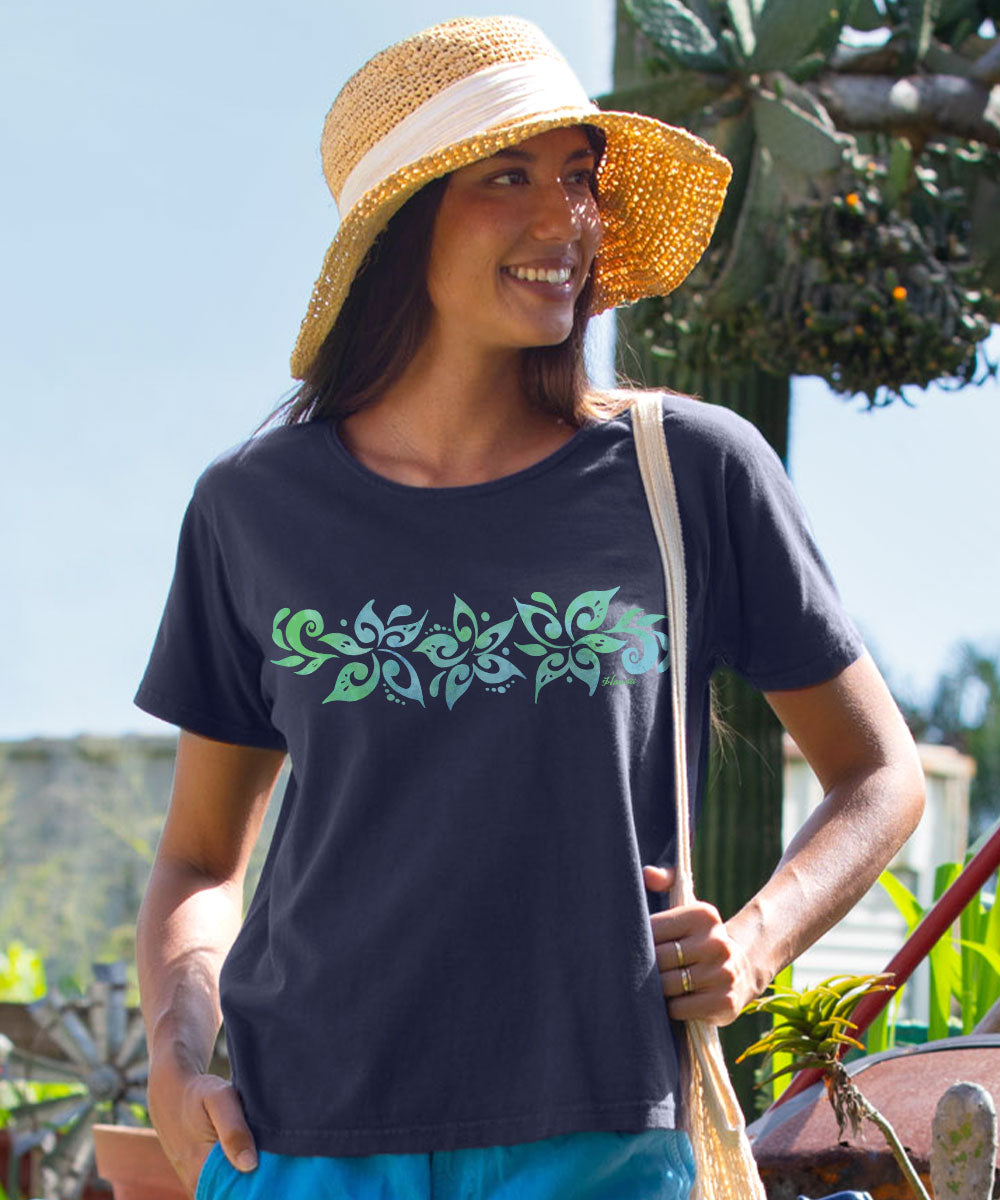 A woman wearing a dark charcoal gray t-shirt with a green and teal floral pattern across the chest, a straw sun hat, and blue pants, standing outdoors. View 2