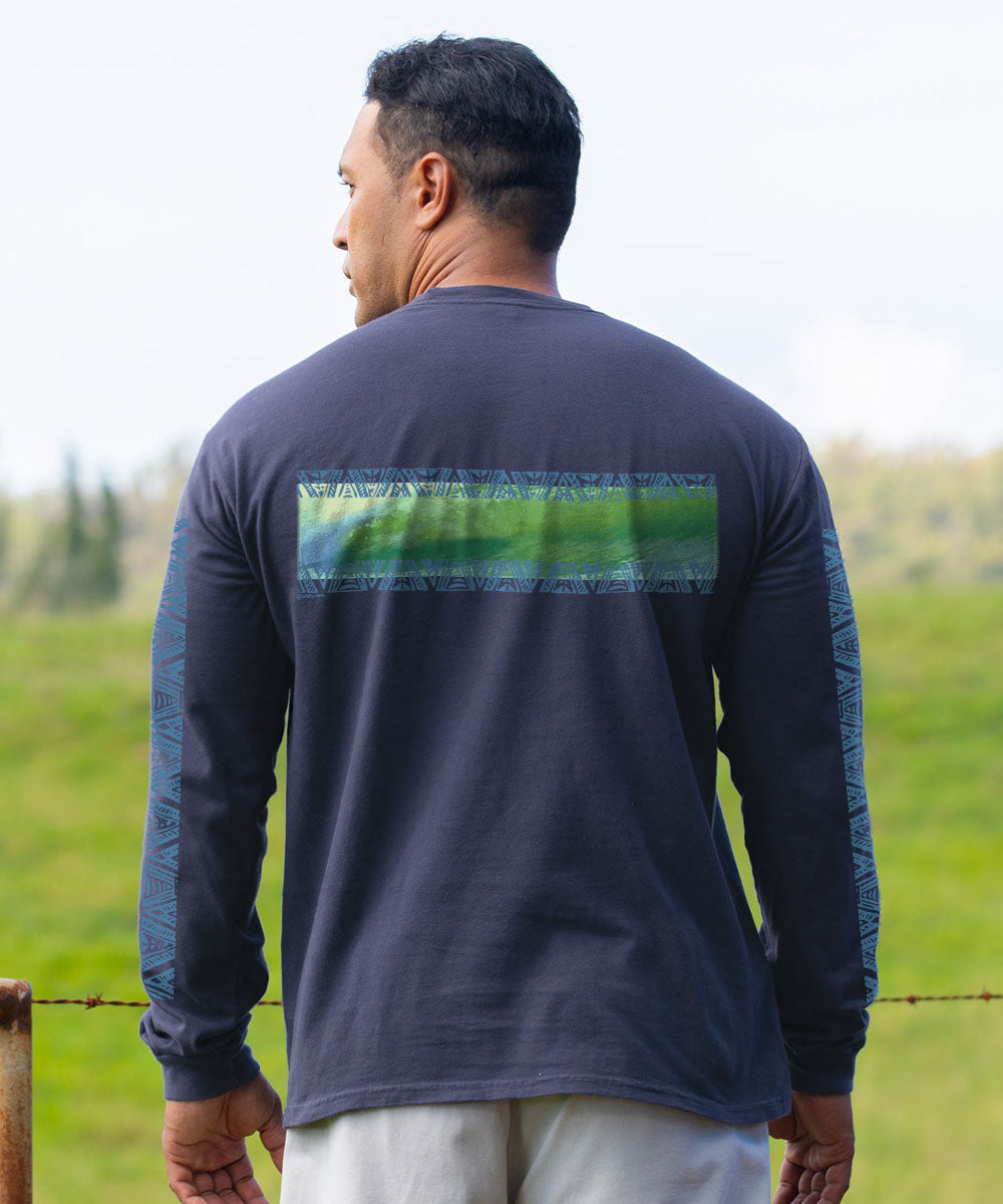A man viewed from behind wearing a dark navy long-sleeve shirt with a green and blue textured horizontal stripe across the upper back and patterned sleeves, standing outdoors in a grassy field. View 3