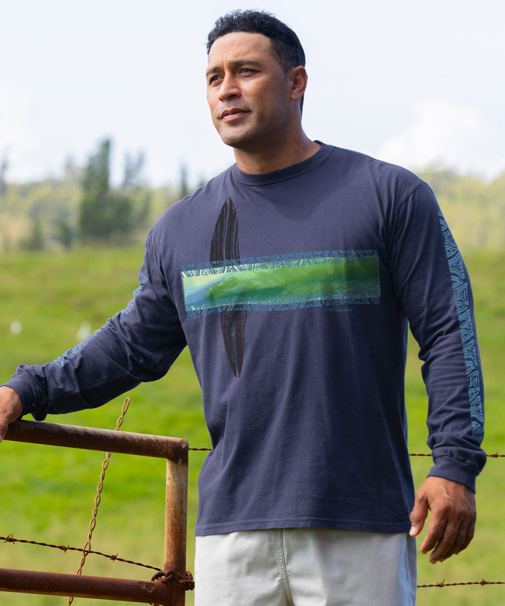 A man wearing a dark navy long-sleeve t-shirt with a green and blue graphic print on the chest, standing outdoors in a grassy field. View 2