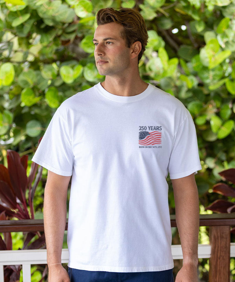 Man wearing a white t-shirt with a graphic design in front of green foliage View 3