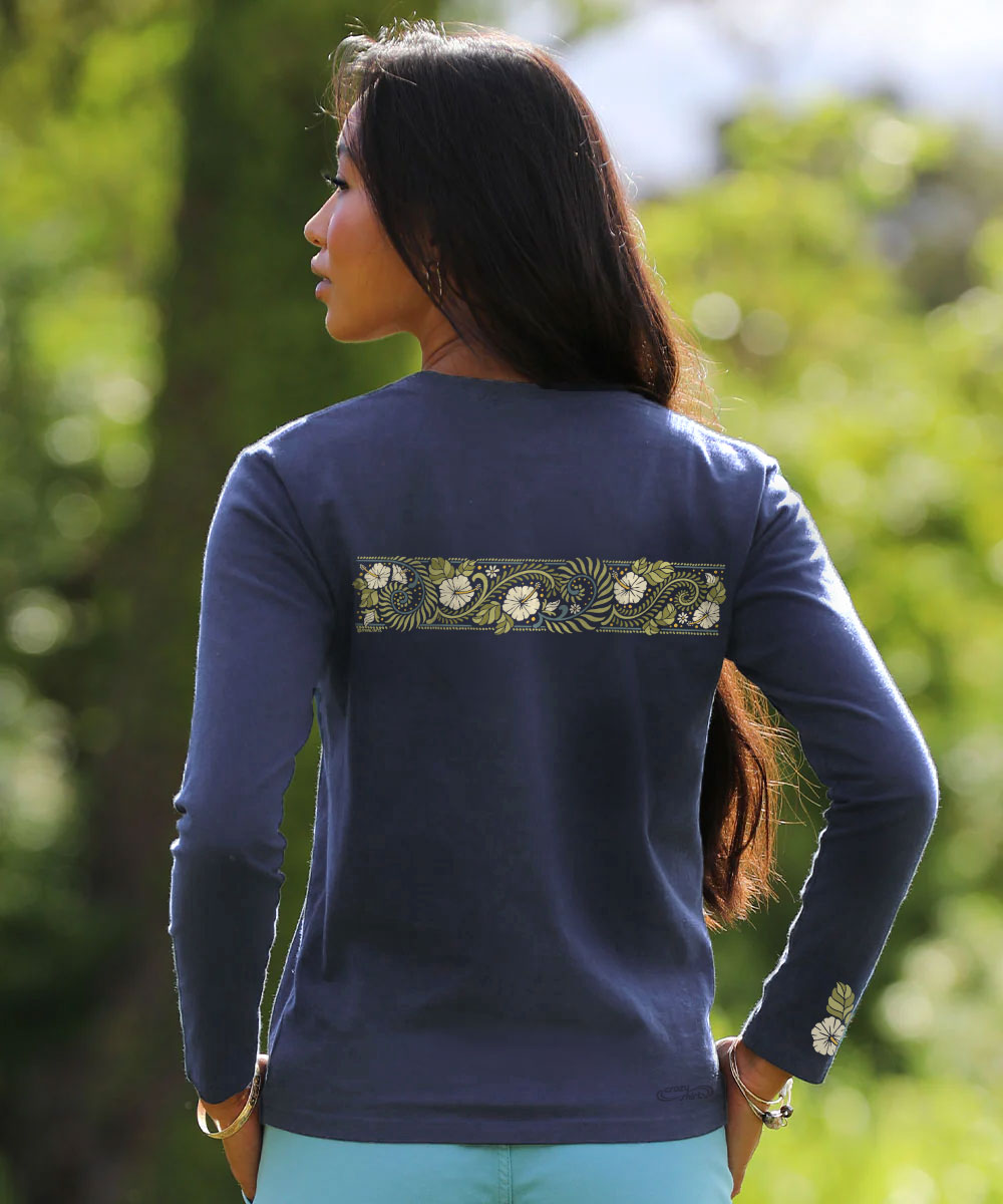 A woman shown from the back wearing a dark navy long-sleeve top with a horizontal floral embroidered band across the upper back and a matching floral detail on the left sleeve, set against a blurred green outdoor background. View 3