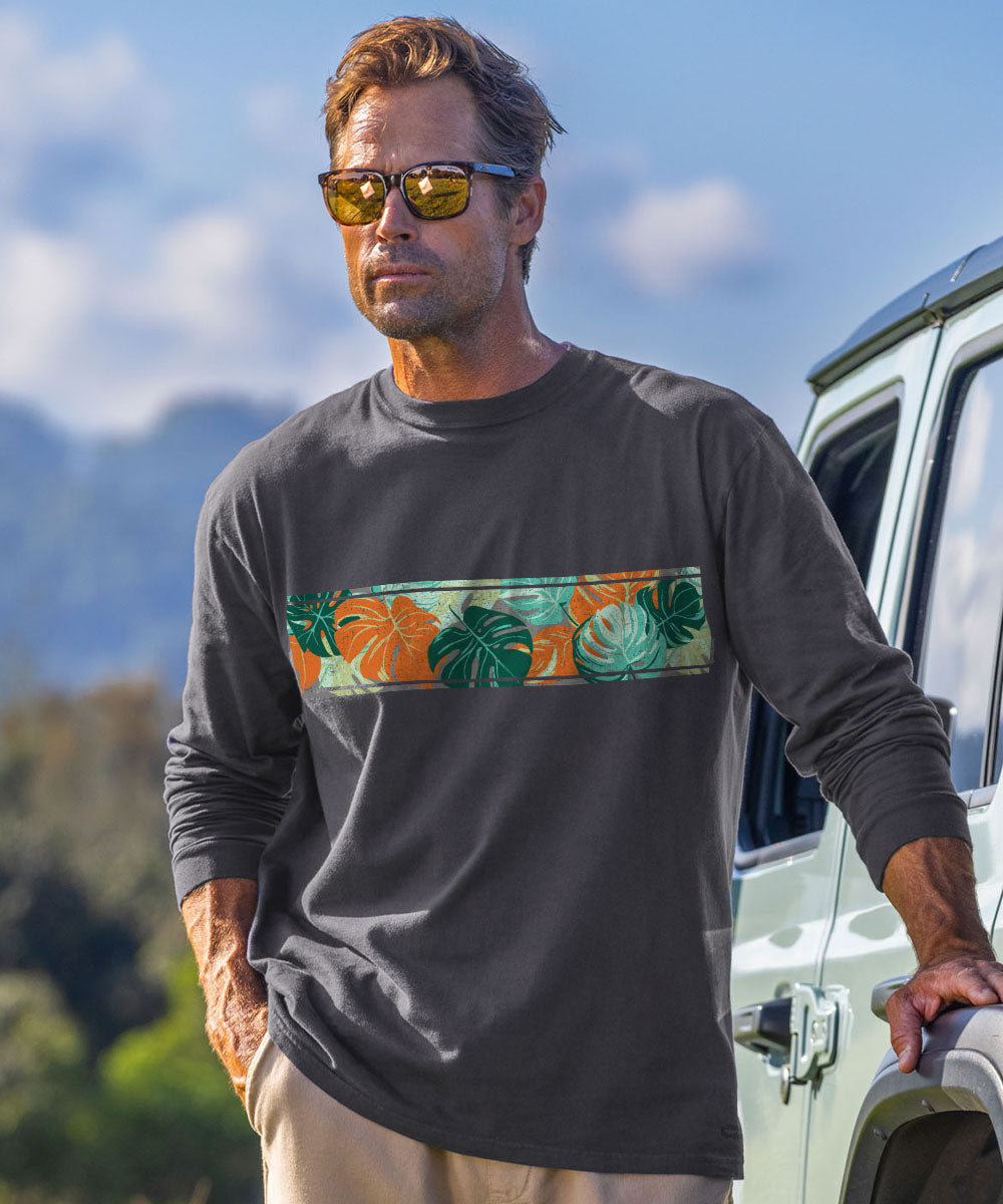 A man wearing a dark charcoal long-sleeve t-shirt with a colorful tropical leaf pattern horizontal band across the chest, standing outdoors next to a white vehicle. View 2