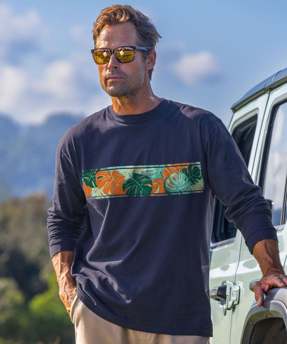 A man wearing a dark charcoal long-sleeve t-shirt with a colorful tropical leaf pattern horizontal band across the chest, standing outdoors next to a white vehicle. View 2