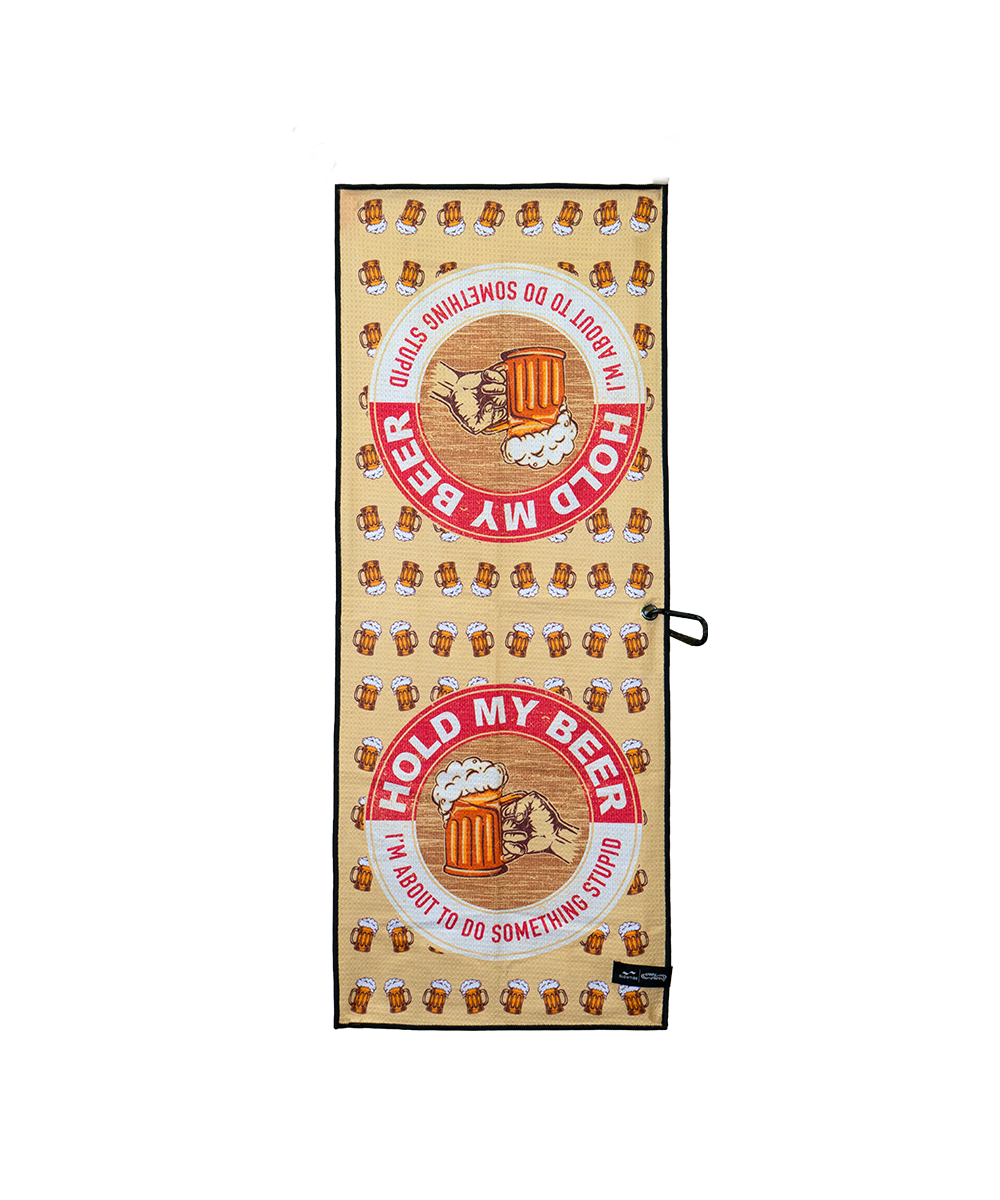 A rectangular beige towel with a black border, featuring a repeating pattern of brown beer mugs and two large circular red and white 'HOLD MY BEER' graphics with a cartoon bear holding a beer mug. A small black tag is visible at the bottom right. View 1