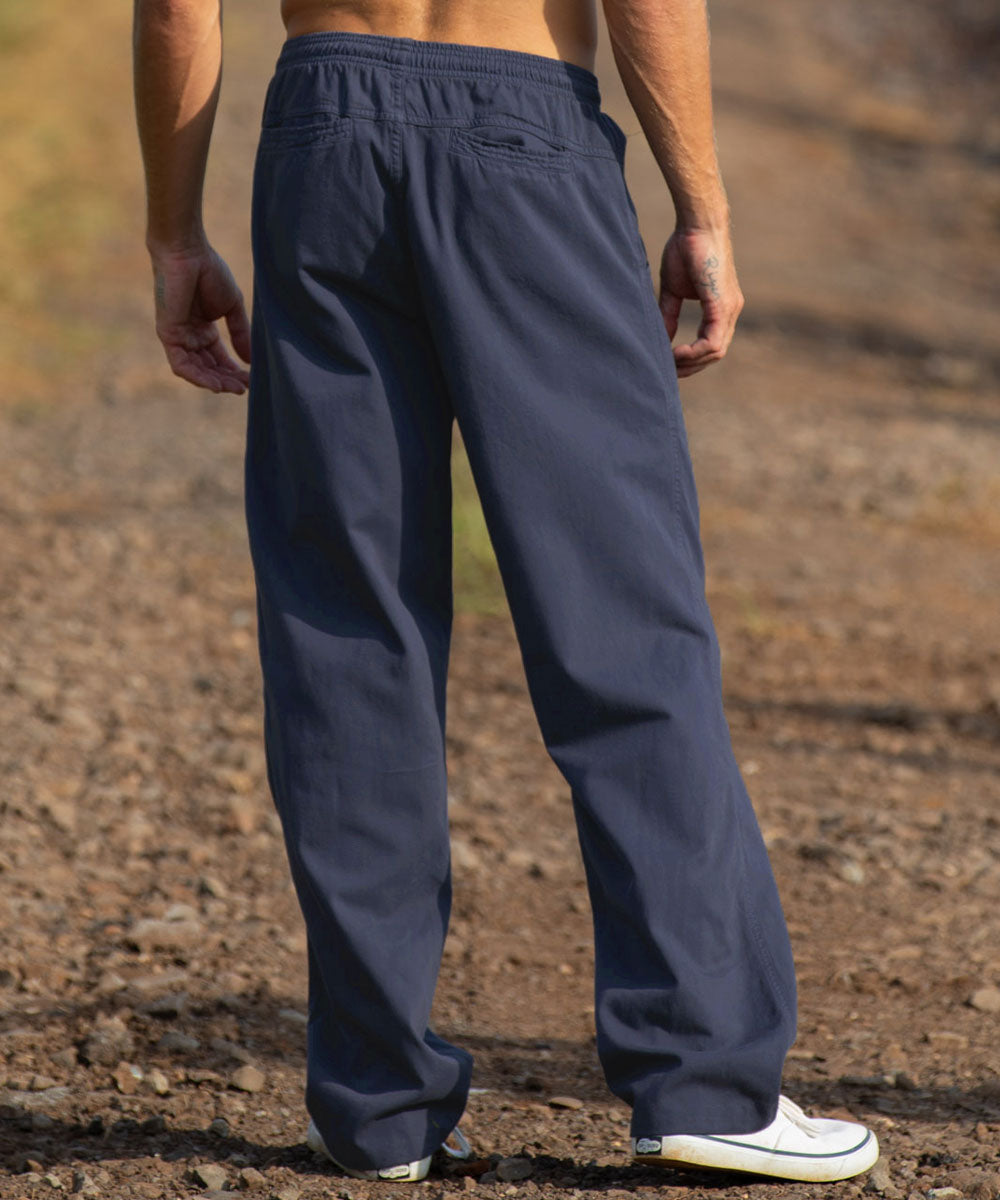 A person shown from the back wearing dark charcoal gray wide-leg pants, standing outdoors on a gravel path. View 3