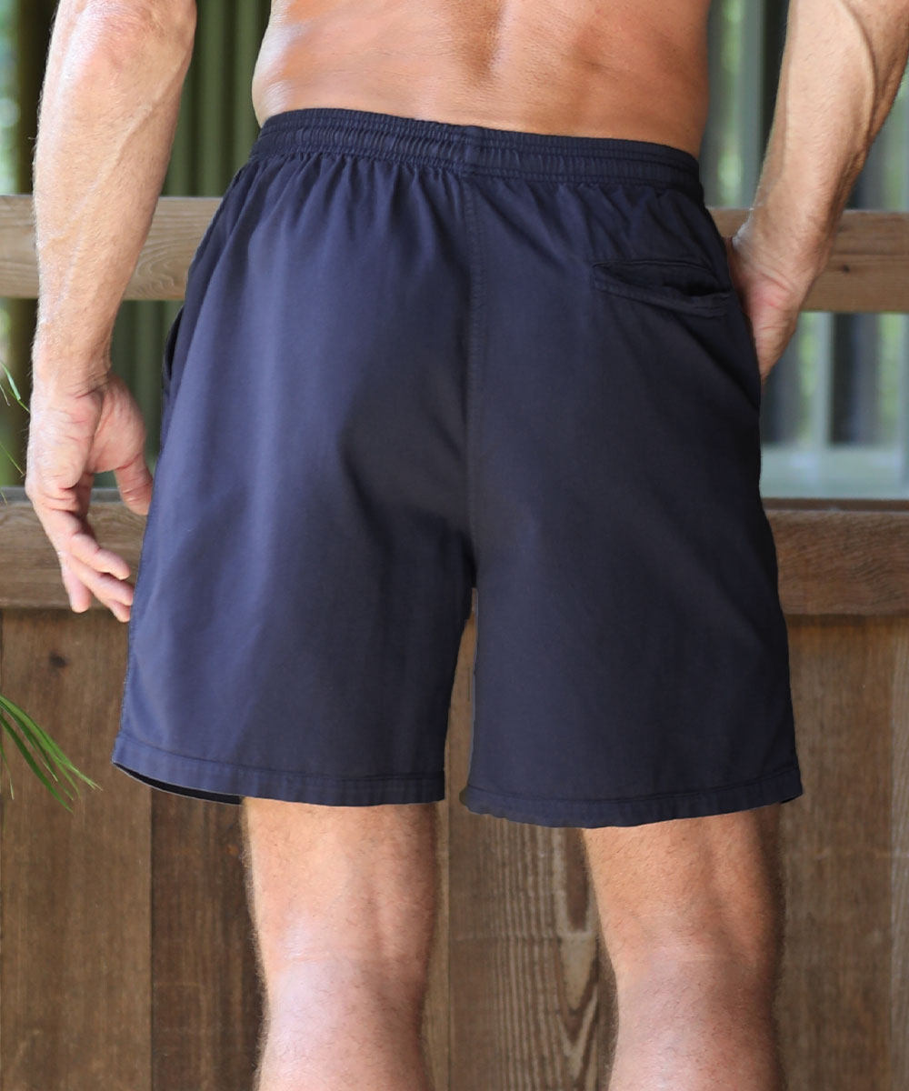 A man wearing dark gray athletic shorts, shown from the back, standing outdoors against a wooden fence. View 3
