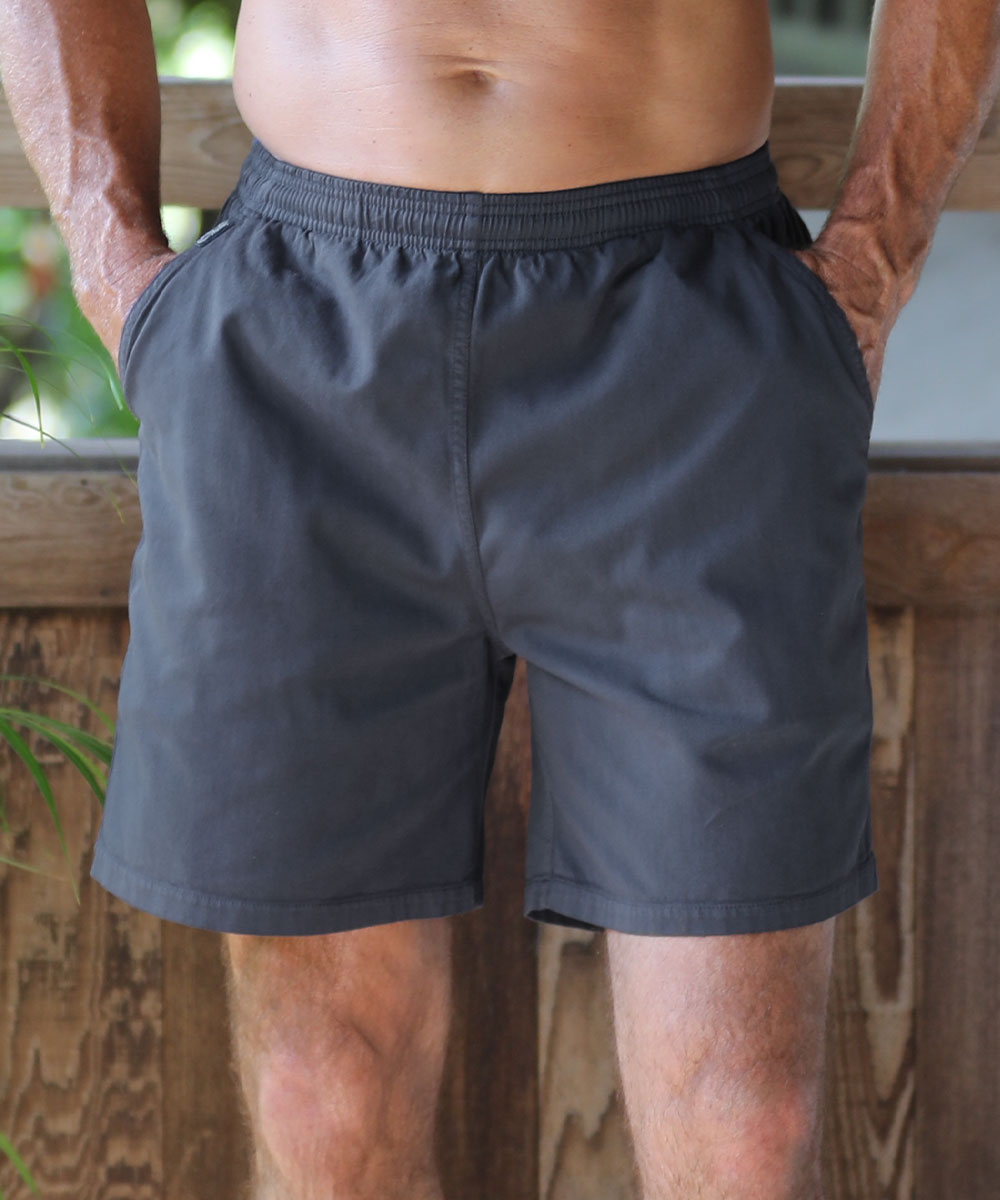 A man wearing dark gray athletic shorts with side pockets, standing in front of a wooden fence. View 2