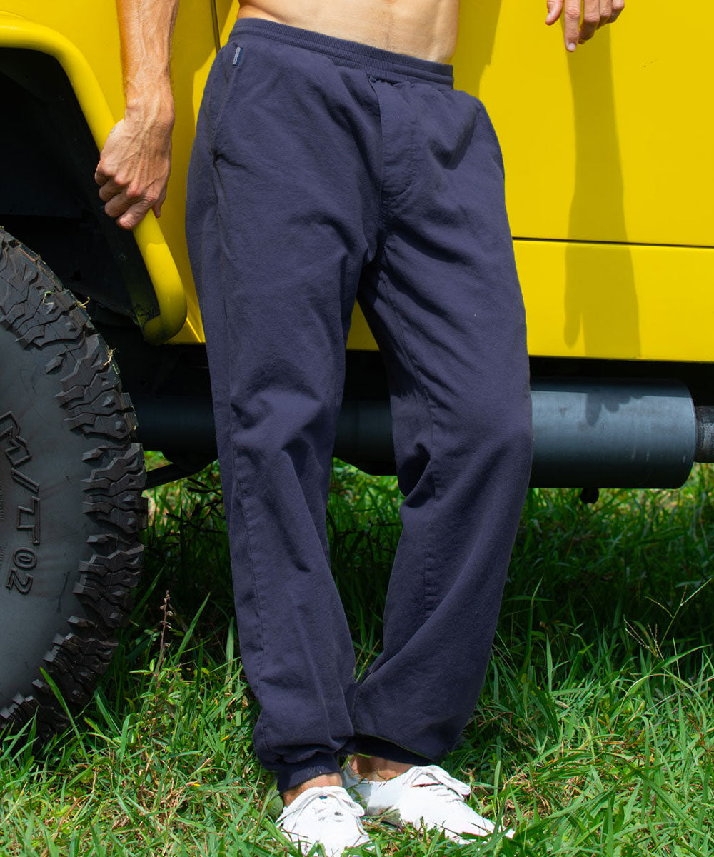 A person standing outdoors on grass beside a bright yellow vehicle, wearing dark charcoal gray jogger-style pants with a back pocket and white sneakers. View 2