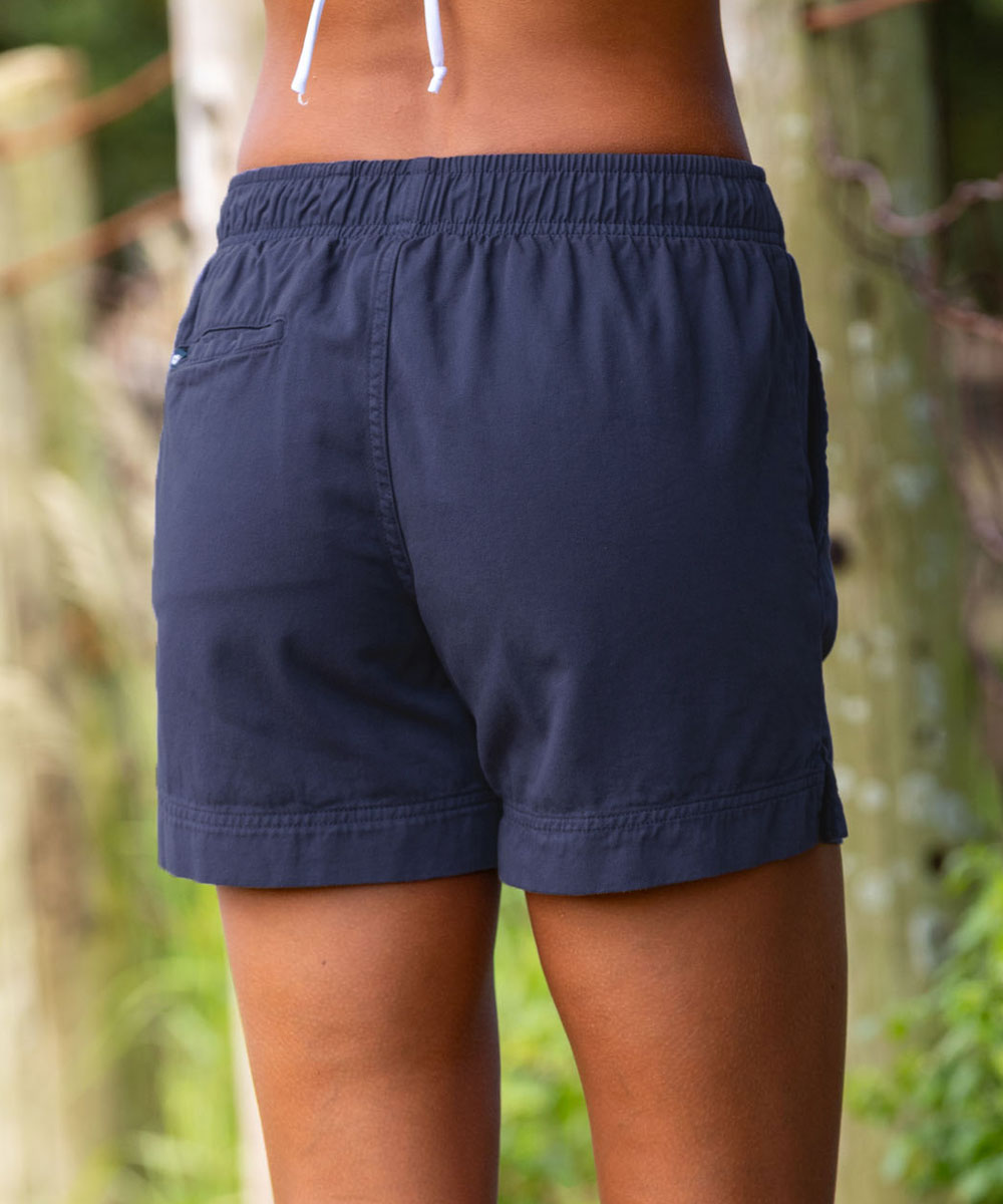 Rear view of a person wearing dark navy drawstring shorts outdoors, with a blurred natural background of trees and foliage. View 3
