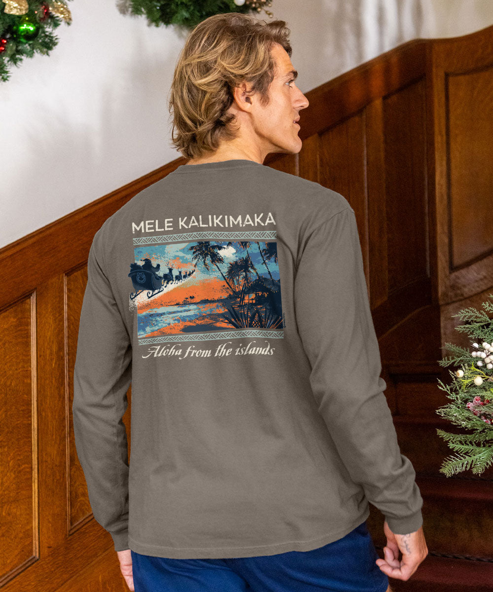 A man wearing a taupe long-sleeve t-shirt, viewed from behind to show the back graphic. The graphic features a tropical sunset scene with the text 'MELE KALIKIMAKA' and 'Aloha From the Islands'.