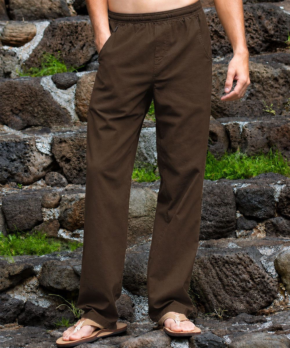 A person wearing light beige drawstring pants and tan sandals, standing on dark volcanic stone steps with green moss in the background. View 2