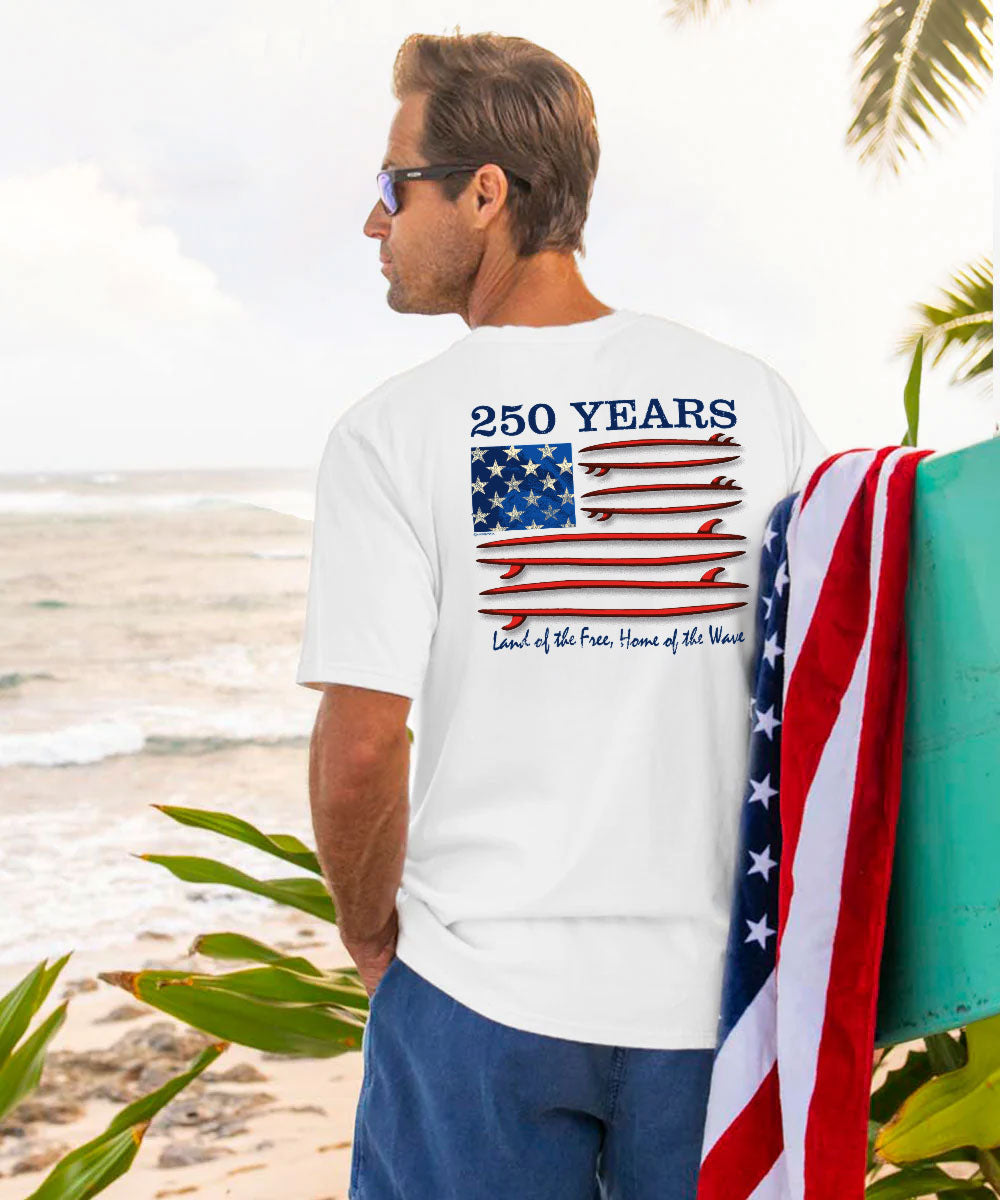 Man on a beach wearing a white t-shirt with a graphic design, holding an American flag. View 2