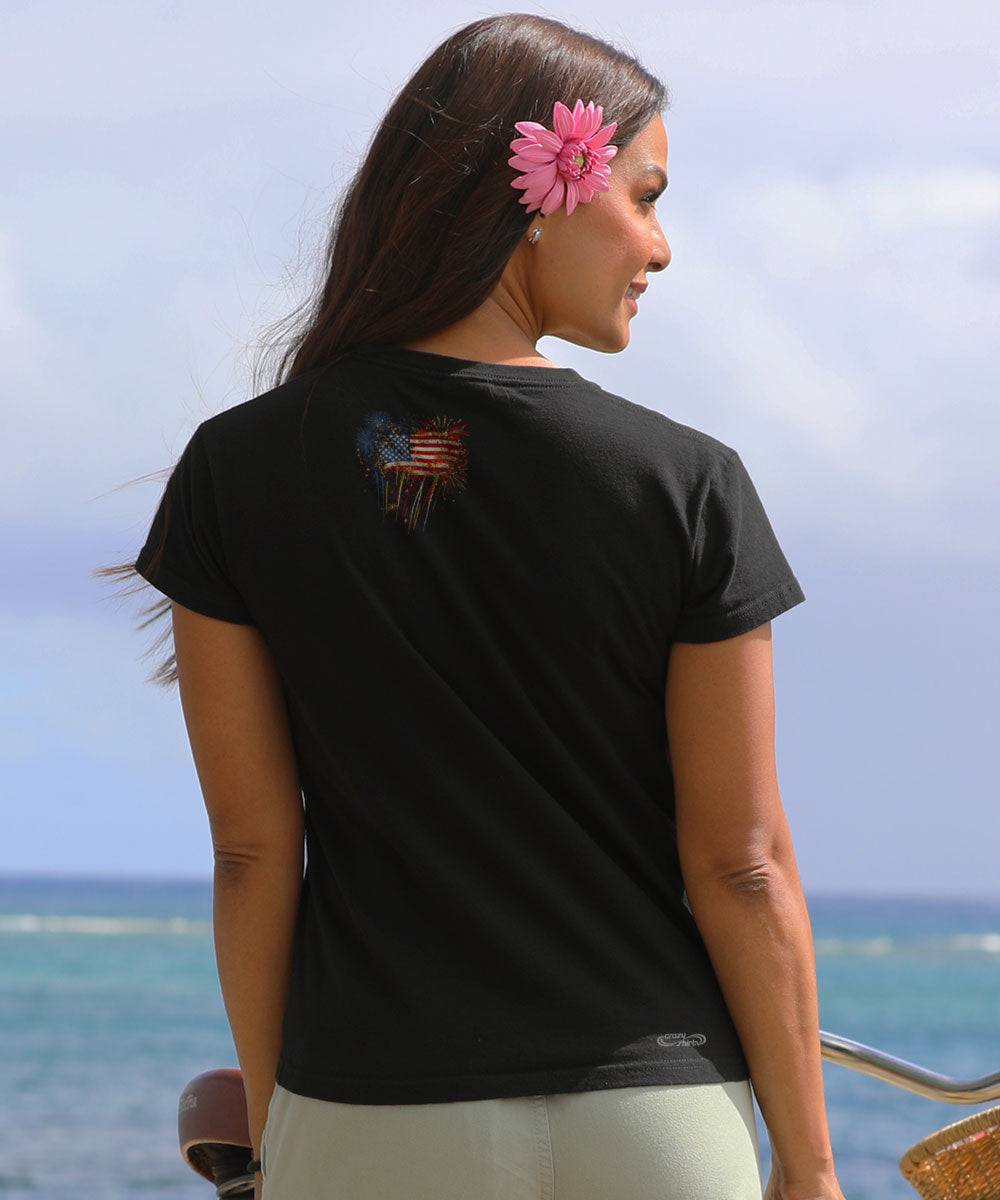 Woman wearing a black t-shirt with a design on the back, standing by the ocean. View 3