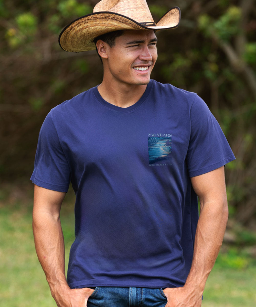 Man wearing a blue t-shirt with a logo and a cowboy hat outdoors. View 3