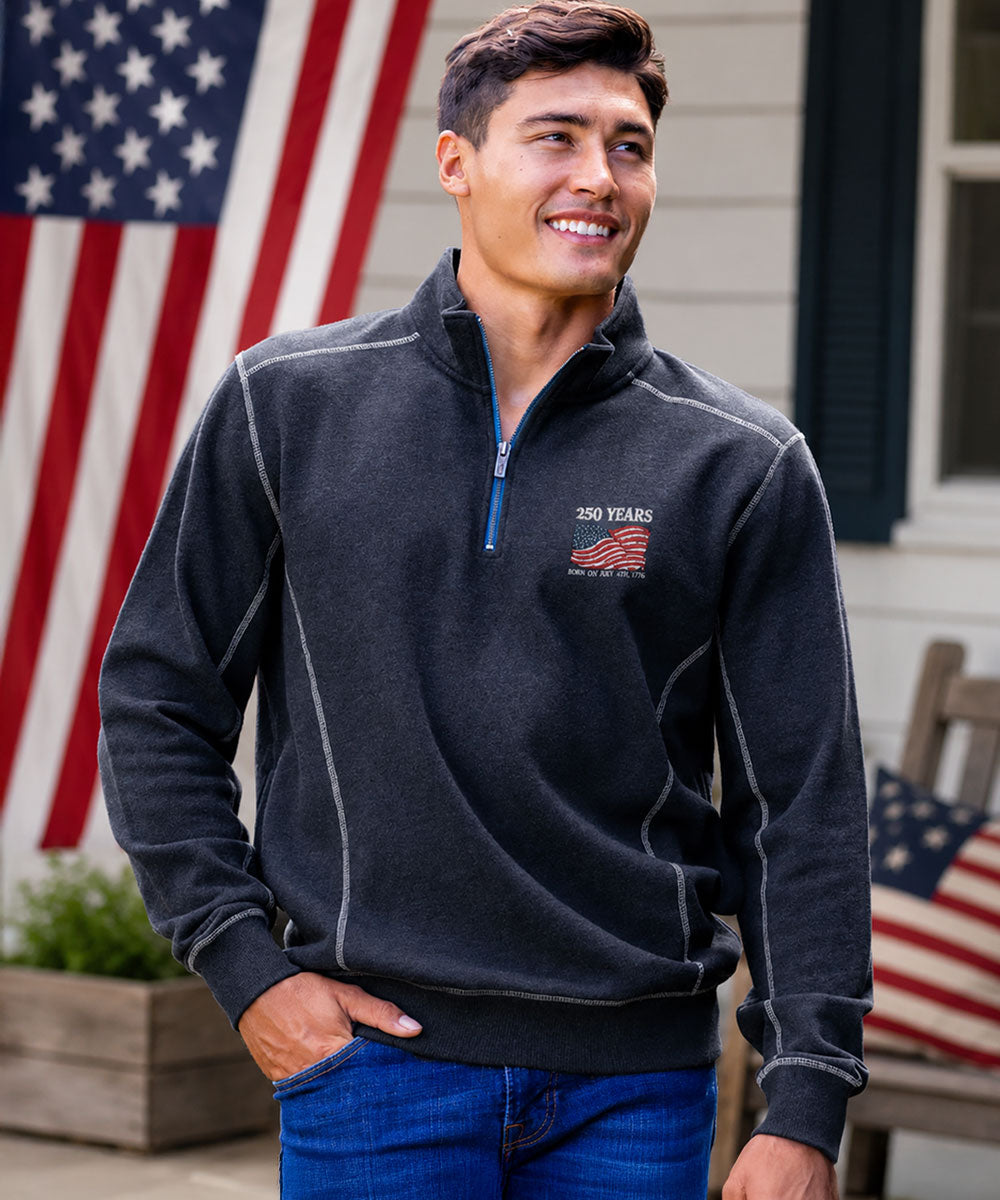 Man wearing a dark blue pullover with a logo in front of an American flag View 2