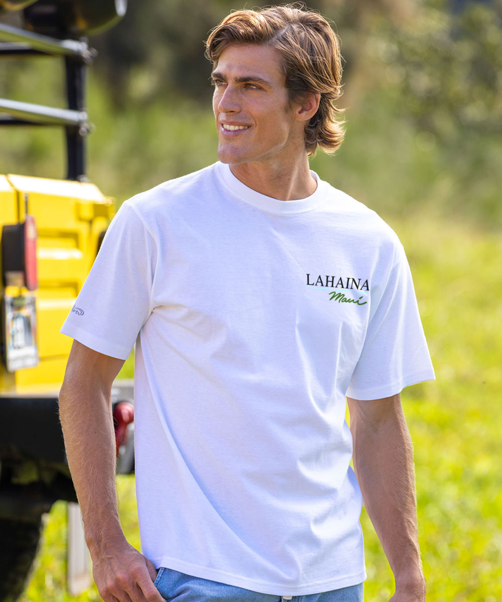 A man wearing a white short-sleeve t-shirt with 'LAHAINA Marine' printed in black on the left chest, standing outdoors in a grassy field next to a yellow vehicle. View 3