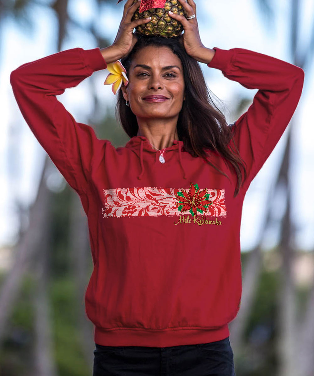 A woman wearing a red long-sleeve hoodie with a white and red floral chest graphic and 'Merry Christmas' text, posing outdoors with a pineapple balanced on her head. View 2