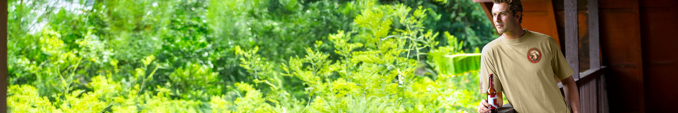 Man wearing Beer Dyed tee standing on a porch looking at a forest