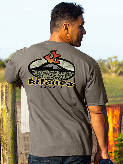 A man wearing a dark gray t-shirt with a large graphic on the back of Kilauea volcano with Kilauea hawaii words below. Standing outdoors next to a wooden fence post.