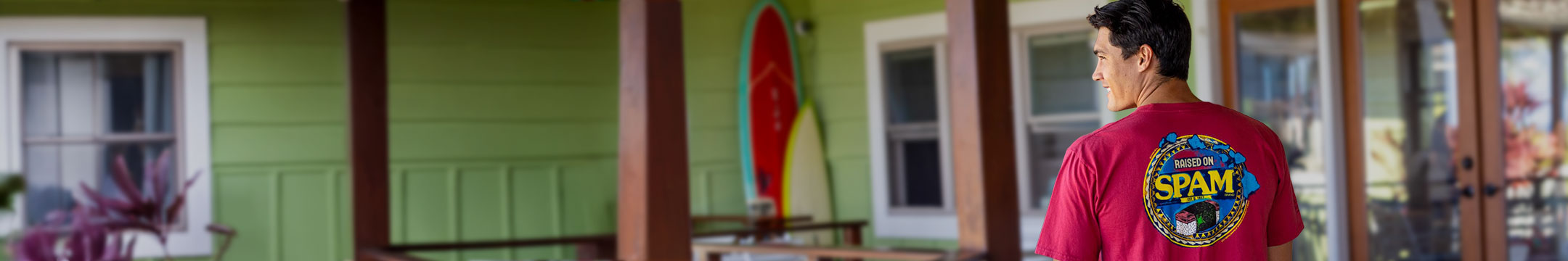 Person wearing a red shirt with a visible brand logo in front of a house with surfboards.