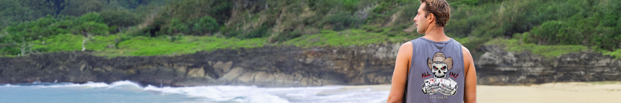Man standing on a beach with ocean waves and greenery in the background