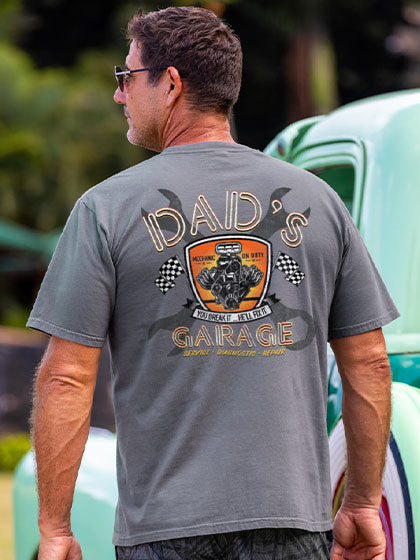 Man wearing a gray t-shirt with 'Dad's Garage' design, standing in front of a vintage car.