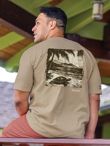 Man wearing a beige t-shirt with a graphic design of a turtle and palm trees, sitting on a wooden bench.