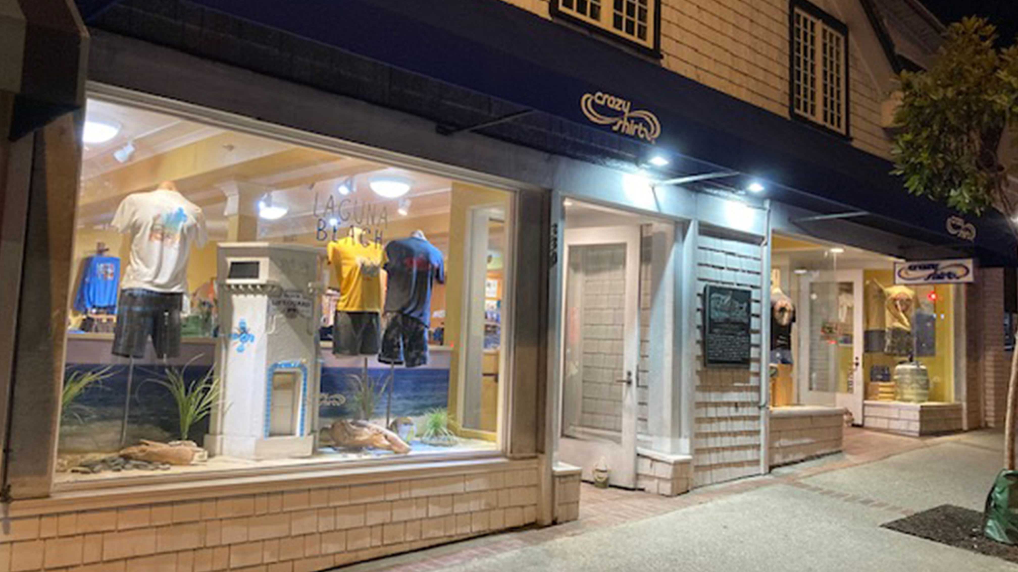 Laguna Beach Storefront with illuminated window display and 'Crazy Shirts' sign at night.