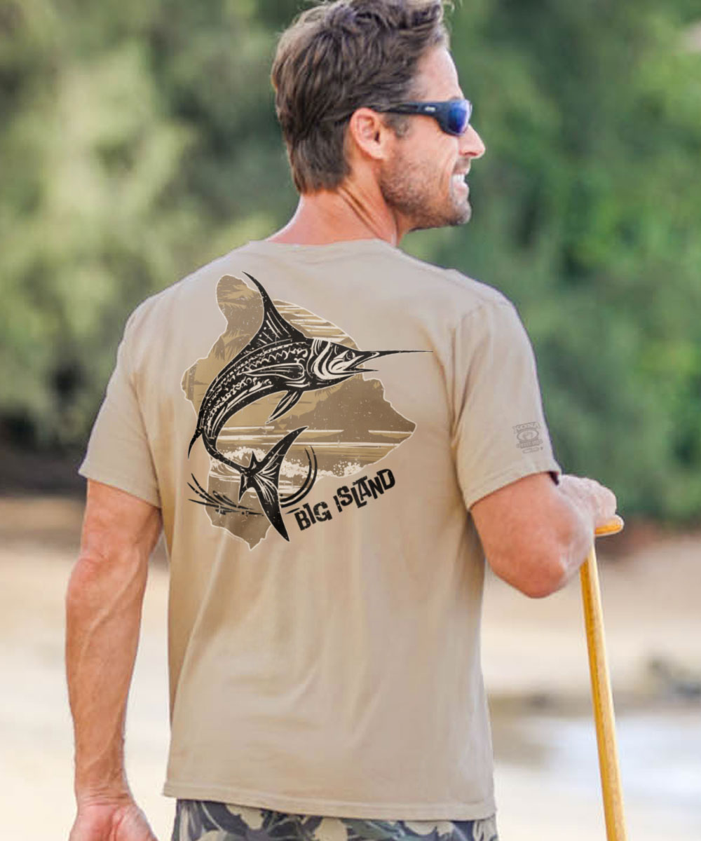 A man facing away from the camera wears a beige short sleeve crewneck t-shirt with a marlin fish design and the text 'Marlin Of Hawaii - Kona Coffee Dyed' on the back. View 2