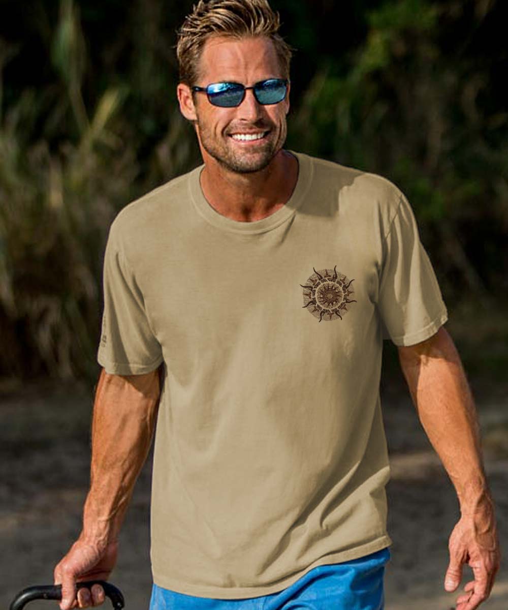 Man wearing a beige crewneck t-shirt with a small sun spinner design on the chest walking on the beach. View 3