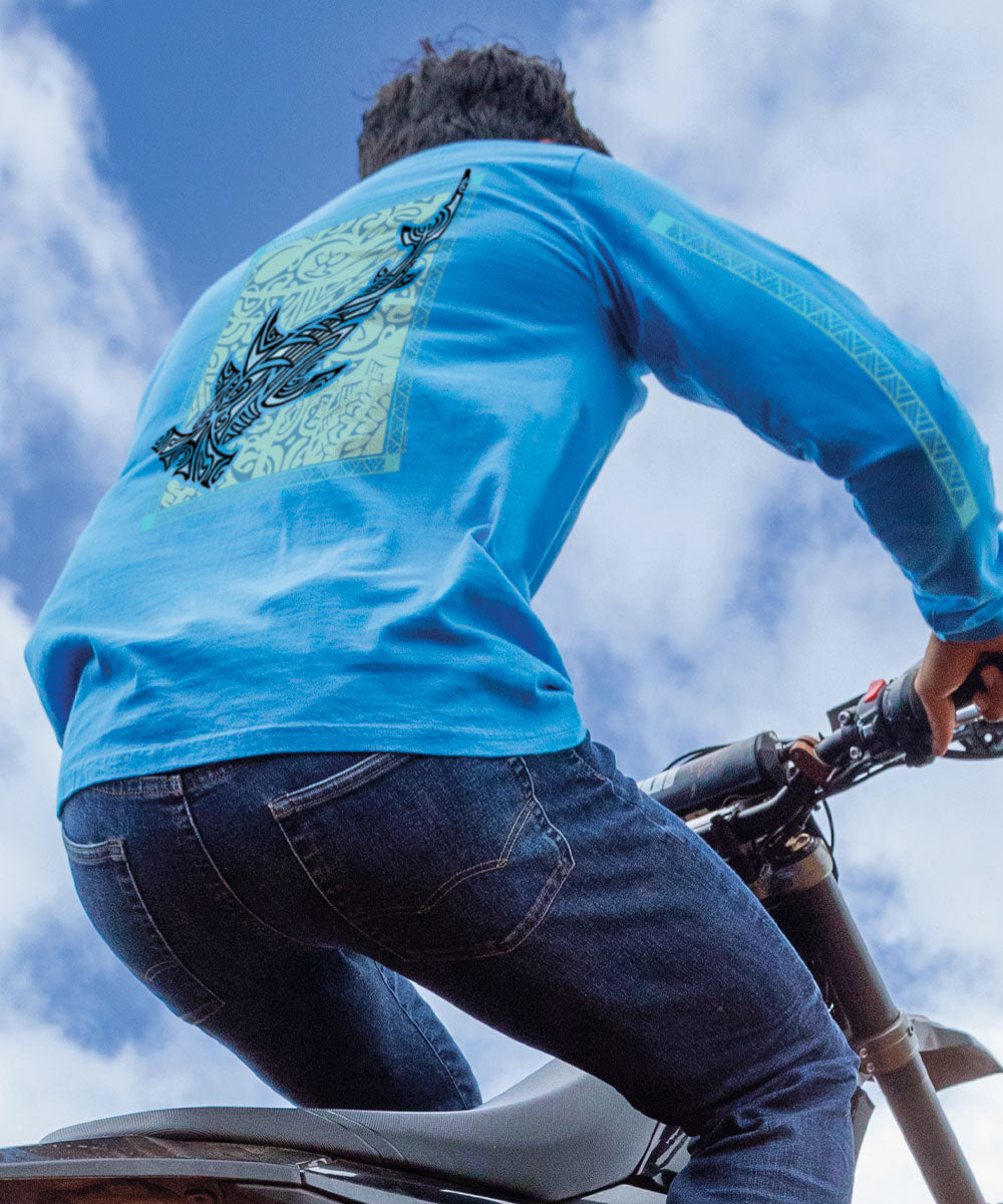 A person riding a motorcycle wearing a blue long sleeve crewneck t-shirt with a tribal hammerhead shark graphic on the back. View 2