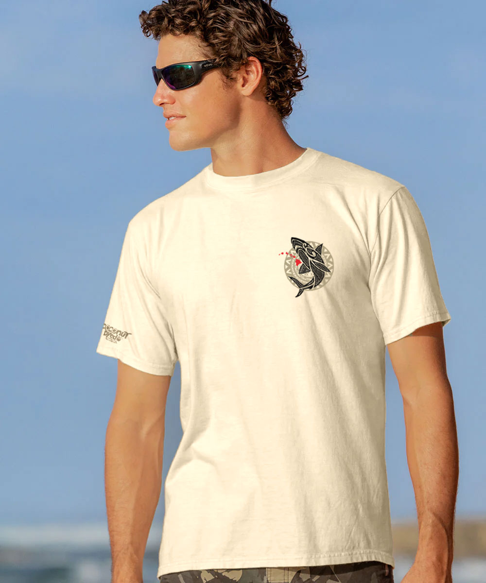 Man in a beige t-shirt with small black logo on chest standing on a beach View 3