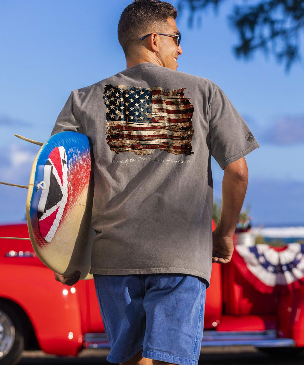 A person wearing a gray short sleeve crewneck t-shirt with an American flag design on the back, standing in front of a red vehicle. View 2