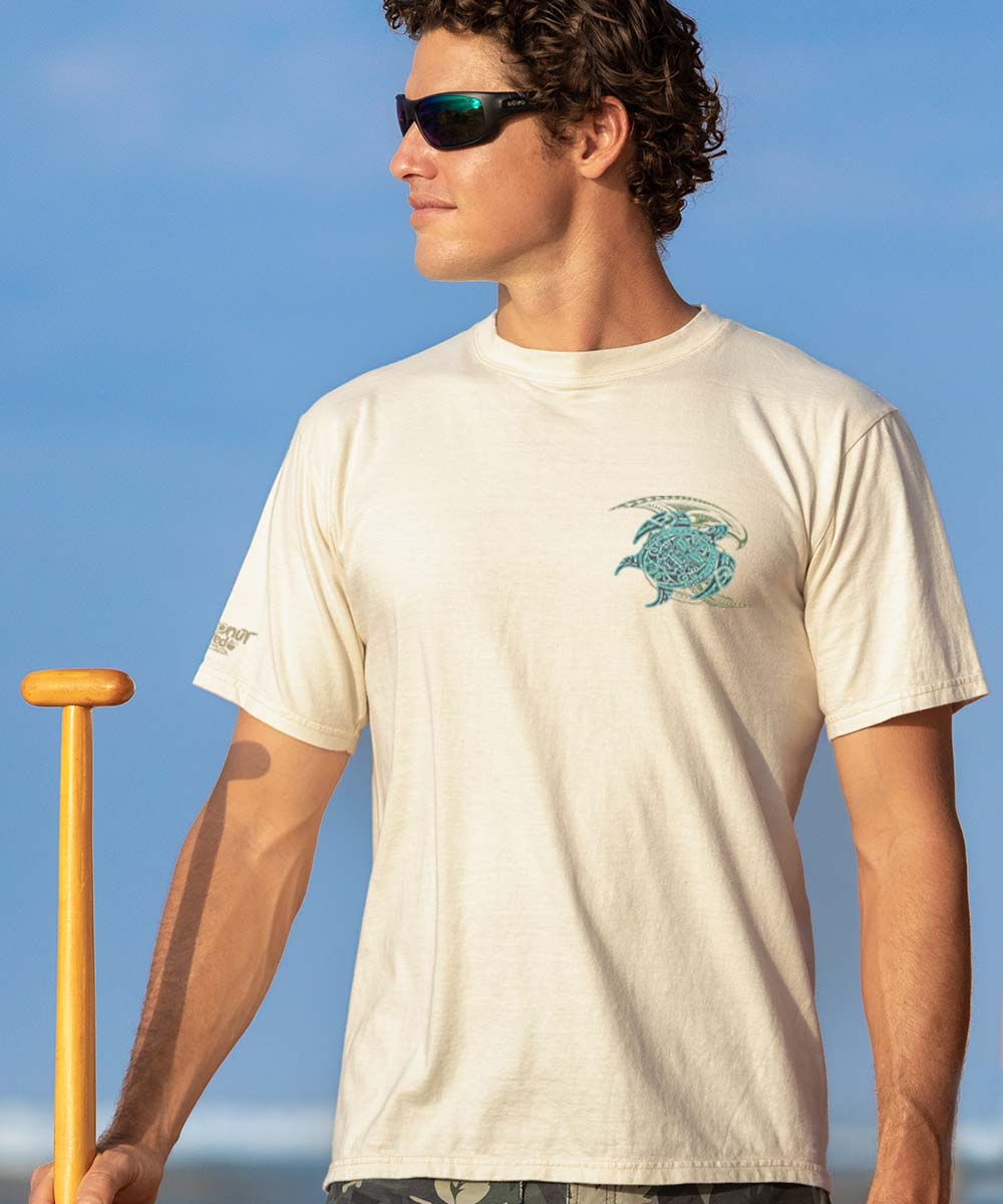 Man wearing a beige short sleeve crewneck t-shirt with a small tribal sea turtle design in blue and green View 3