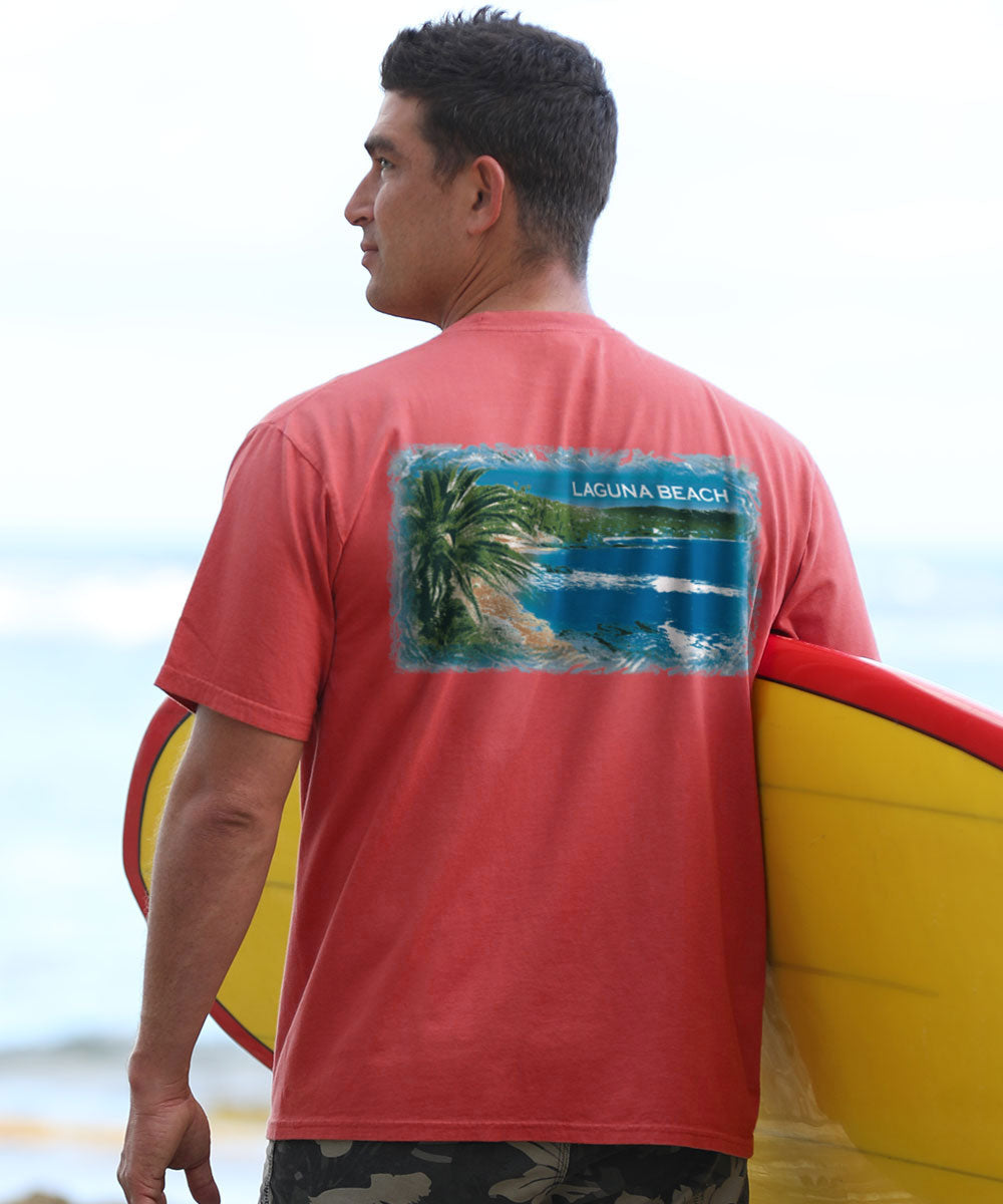 A person facing away from the camera wears a red crewneck t-shirt with a scenic print of Laguna Beach, holding a surfboard. View 2