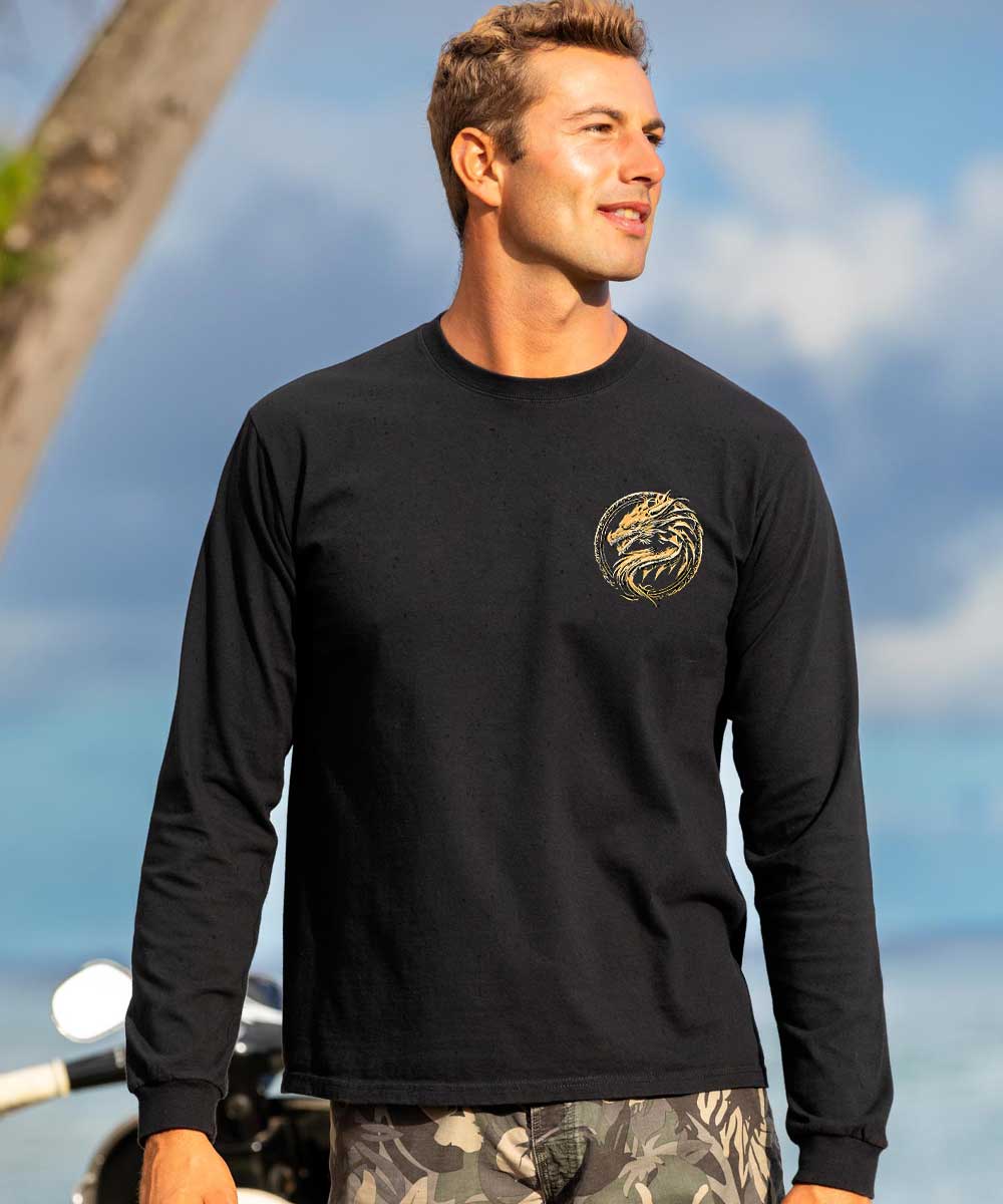 A man wearing a black long-sleeve shirt with a gold graphic on the chest with blurred sky in the background. View 3