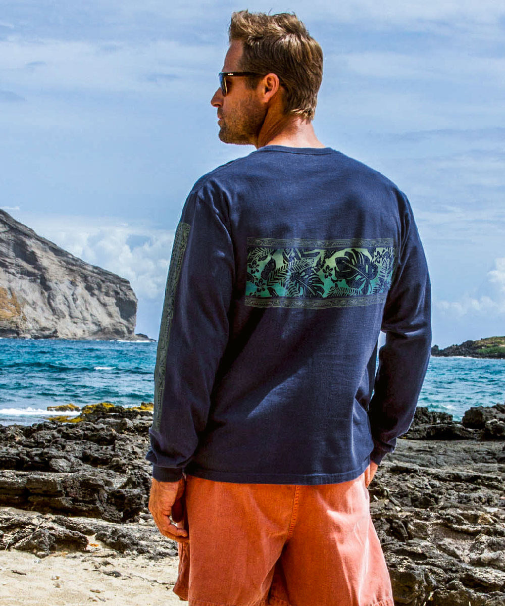 A man wearing sunglasses and a navy long sleeve crewneck t-shirt with a linear rainforest design, standing in front of the ocean View 3