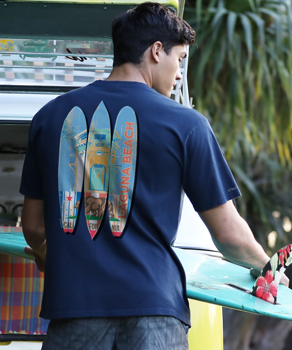 A person wearing a navy blue short sleeve crewneck T-shirt with a graphic of surfboards and the text 'Laguna Beach' on the back. View 2