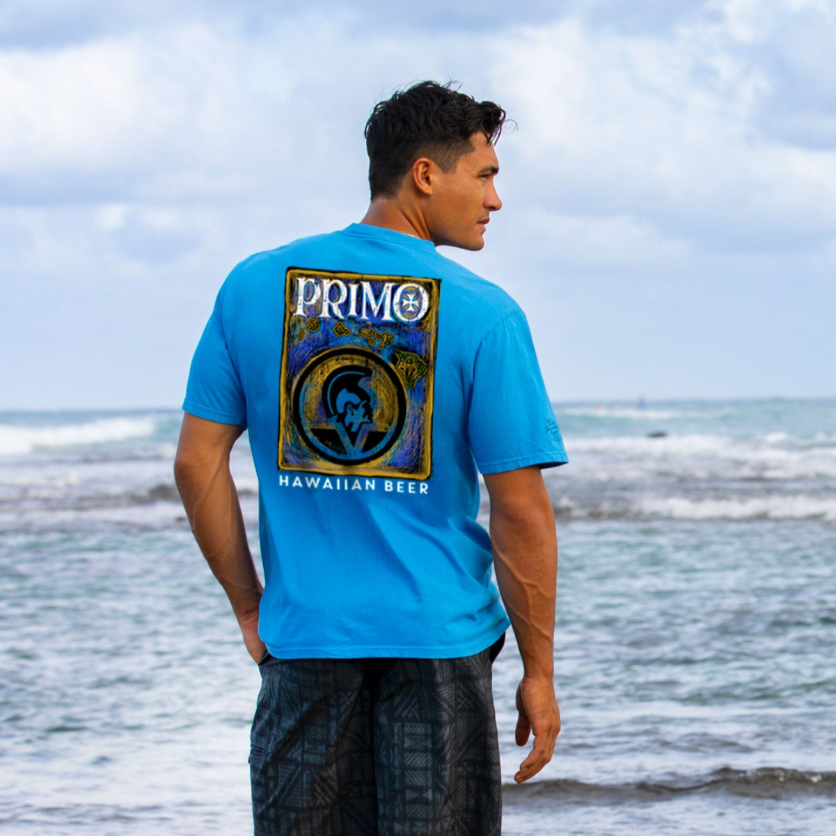 Man wearing a blue Primo Hawaiian Beer t-shirt by the ocean