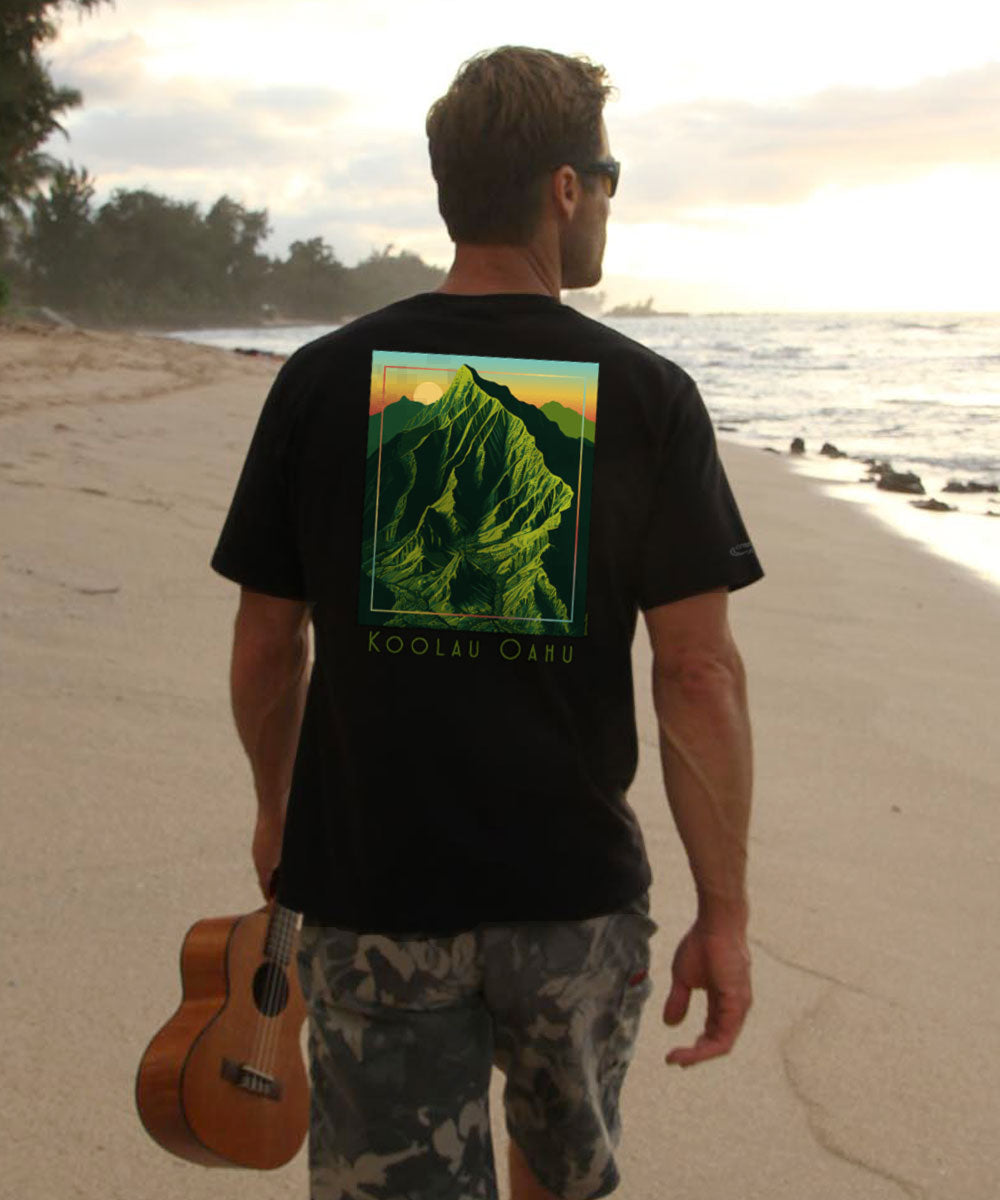 A person standing on a beach at sunset wearing a black short sleeve crewneck t-shirt with a green mountain design on the back. View 2
