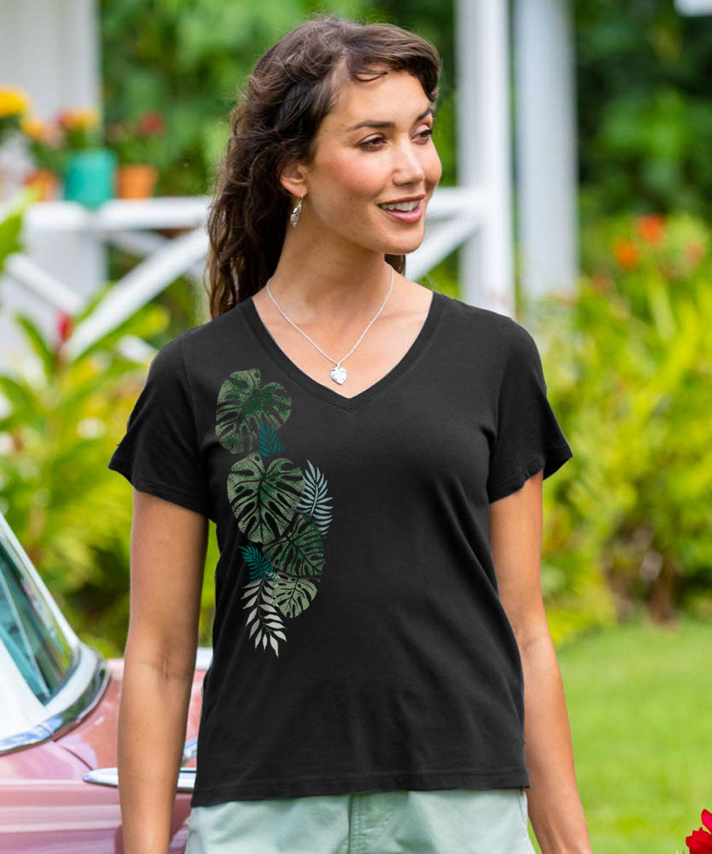 A woman wearing a jet black short sleeve pima v-neck t-shirt with a green tropical leaf design, standing in front of a classic car. View 2