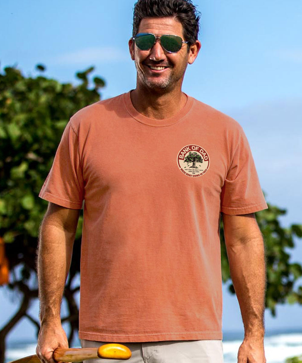 Man wearing a light red t-shirt with a small logo on the chest with some trees in the background. View 3