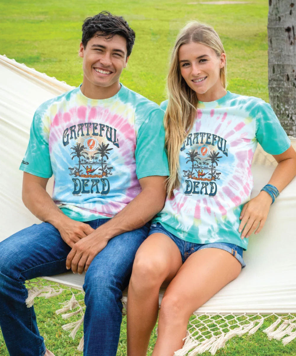 Two smiling people sitting on a bench, wearing tie-dye short sleeve crewneck t-shirts with 'Grateful Dead' text and graphics on them. View 2