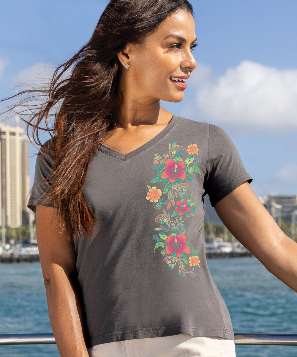 A woman wearing a gray short sleeve Pima cotton V-neck t-shirt with a floral turtle design on the left side, standing on a boat. View 2
