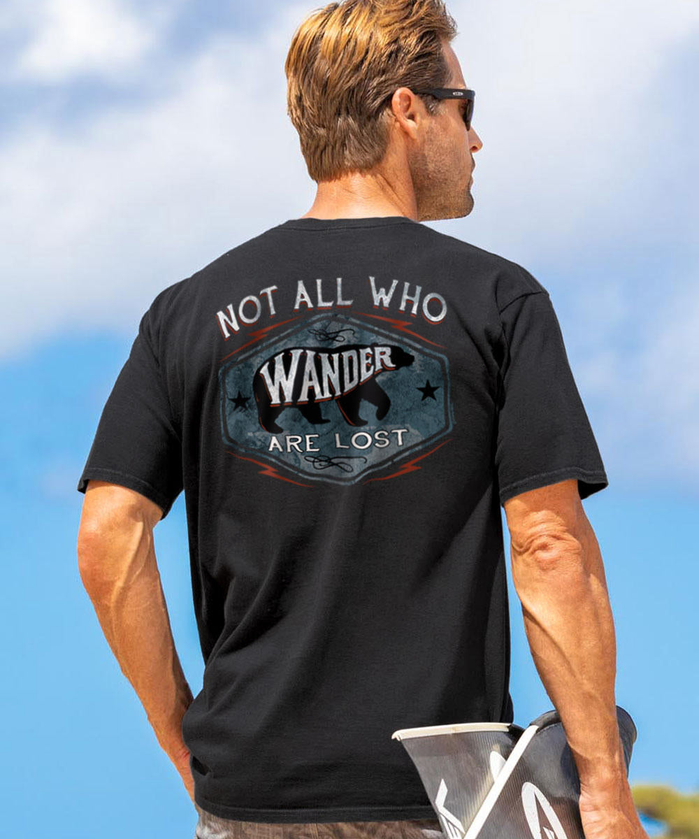 A man wearing a black short sleeve crewneck t-shirt with a graphic text on the back that reads 'Not all who Wander are lost', outdoors. View 2