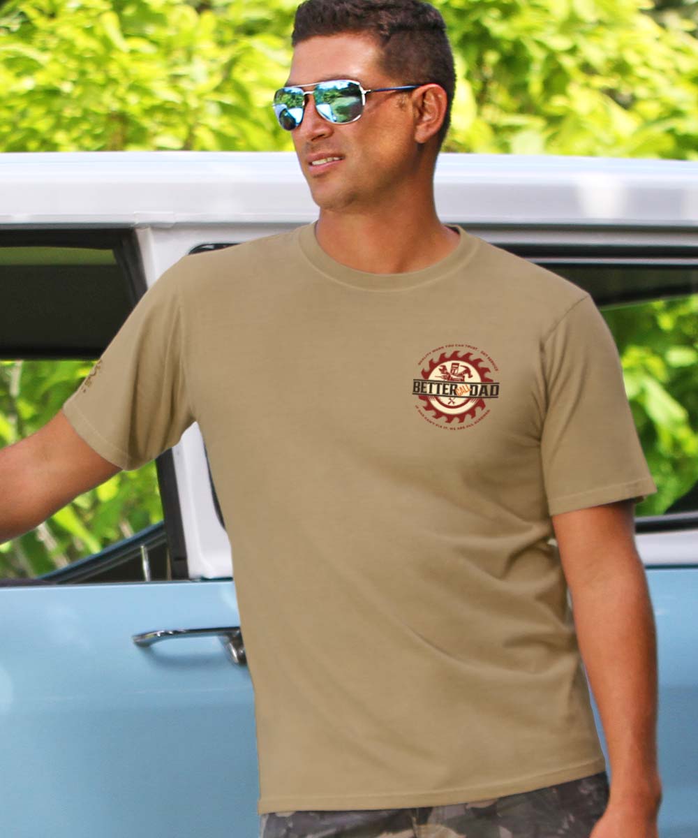 Man leaning against car wearing beige shirt with small logo on chest. View 3