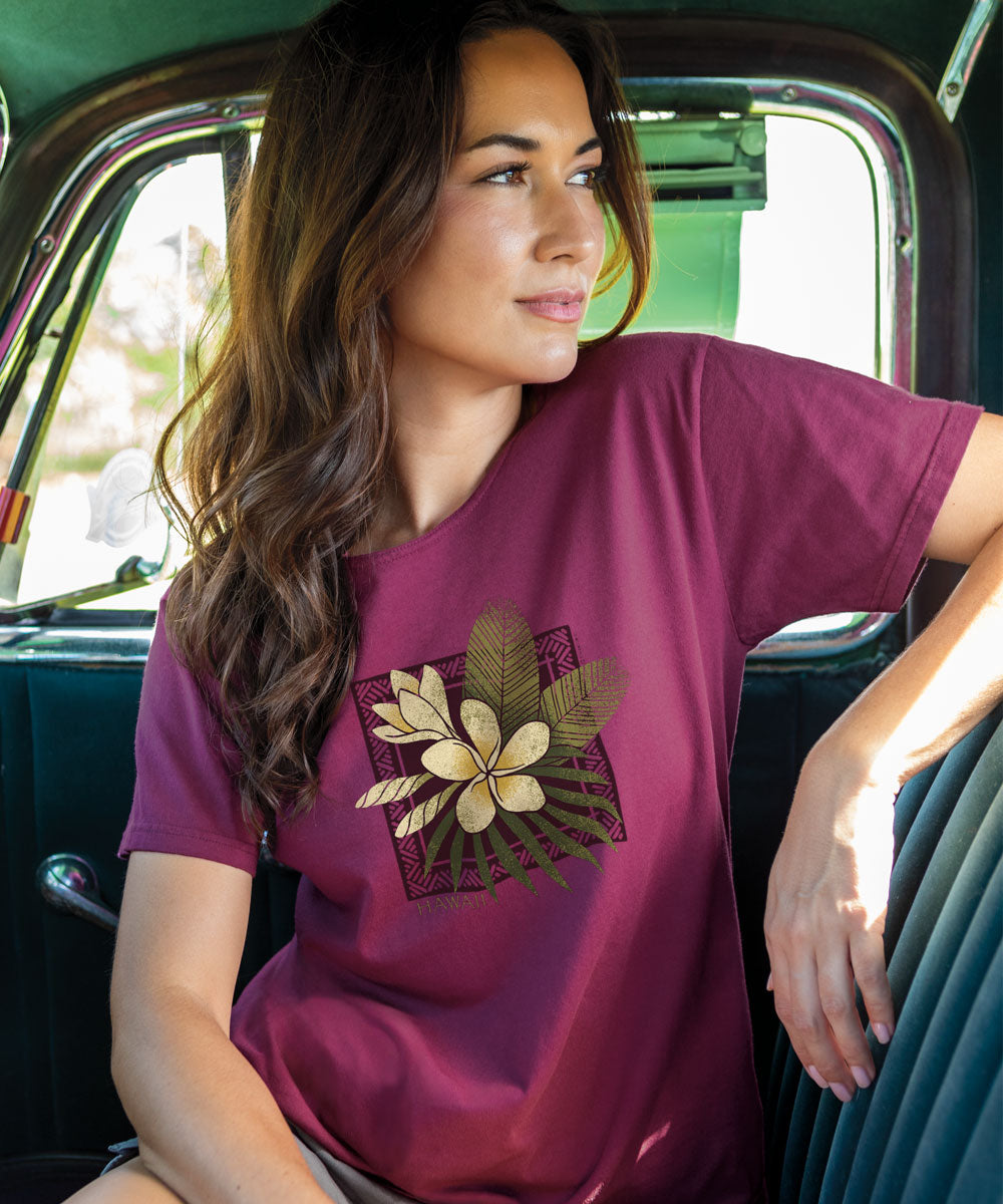 A person wearing a short sleeve scoop neck t-shirt in wine color, with a floral design featuring a plumeria flower on the front. View 2