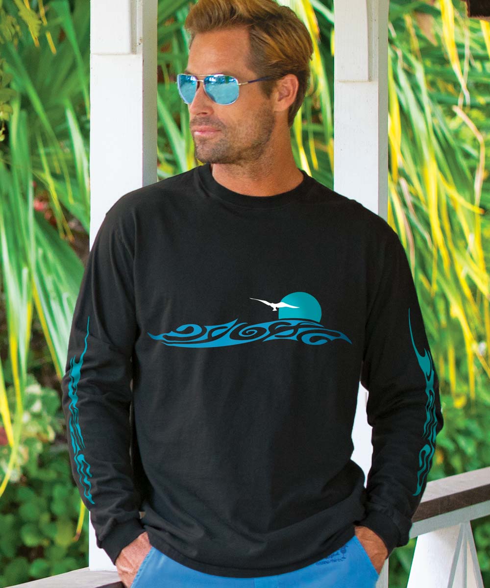 A man wearing sunglasses and a black long sleeve crewneck T-shirt with a blue horizontal tribal design on the front, with greenery in the background. View 2